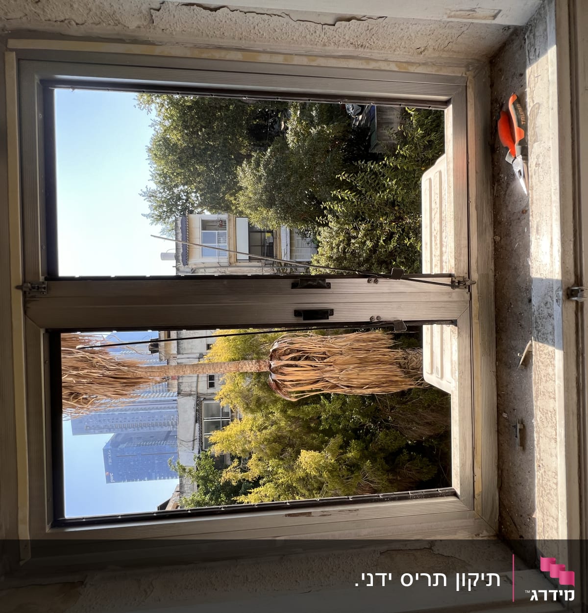 חלון עם תריסים פתוחים וכלי עבודה על אדן החלון